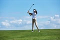 Young woman playing golf on green field against sky and swinging golf club Royalty Free Stock Photo