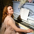 A young woman plays on a blue piano in the rays of light. Female pianist sits near a retro musical instrument with flowers and