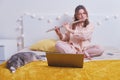 Young woman plays the flute on the bed with a cat, online music lessons. Girl with a musical instrument in her hands in the home