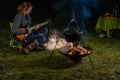 Young woman plays guitar in nature. Kettle is steaming over the campfire. Her tricolor Australian Shepherd watches and listens to