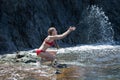 Young woman plays with seawater against dark cliff