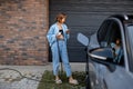 Woman charges her electric car near a house Royalty Free Stock Photo