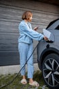 Woman charges her electric car near a house Royalty Free Stock Photo