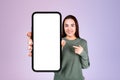 Young woman pointing at big blank phone display on lilac backgro Royalty Free Stock Photo