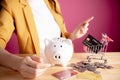 Young woman pointing to empty space with white piggybank,coins and shopping cart or trolley. collecting points a credit card.