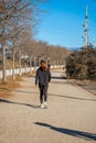 Young woman with a ponytail, dressed in sports clothing and black tights, walking quickly along a path in a public park to consume