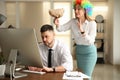 Young woman popping paper bag behind her colleague in office. Funny joke