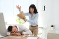 Young woman popping paper bag behind her sleeping colleague. April fool`s day