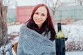 Young woman poses, sitting on street in yard. Female wrapped in grey plaid with alcohol while picnic in winter season.