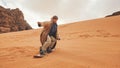 Young woman posing as sand dune surfing wearing bisht - traditional Bedouin coat. Sandsurfing is one of the attractions in Wadi