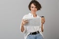 Young woman posing isolated over grey background drinking coffee holding newspaper reading Royalty Free Stock Photo