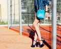 A young woman posing in a jeans outfit, incredible high-heeled shoes and a super-fashioned blue hand bag in a sports park on a sum