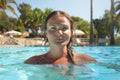 Young woman posing in sun lit tropical resort swimming pool, closeup on head, blurred sunbeds and palm trees background Royalty Free Stock Photo