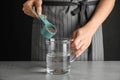 Young woman pouring chia seeds into measuring glass with water at table