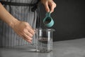 Young woman pouring chia seeds into measuring glass with water at table