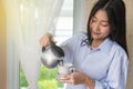 Young woman is pouring coffee from coffee pot into  white cup beside the window in room Royalty Free Stock Photo