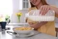 Young woman pouring milk from gallon bottle into plate with breakfast cereal at white marble table in kitchen, closeup Royalty Free Stock Photo