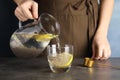 Young woman pouring water with chia seeds and lemon into glass at table