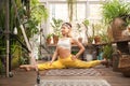 Young woman practices yoga at home among flowers. Biophilia design. Urban jungle and gymnastics, yoga, pilates. Royalty Free Stock Photo