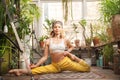 Young woman practices yoga at home among flowers. Biophilia design. Urban jungle and gymnastics, yoga, pilates. Royalty Free Stock Photo