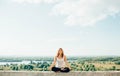 Young woman practices yoga outside. Calm peaceful girl sitting on parapet in lotus position. Her hands lowered to knees