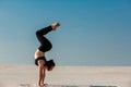 Young woman practicing handstand on beach with white sand and bright blue sky Royalty Free Stock Photo