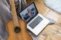 Young woman practicing and learning how to play guitar on laptop computer monitor. Female guitarist watching online