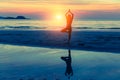 Young woman practicing yoga on the beach at sunset with reflection in water. Royalty Free Stock Photo