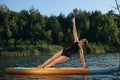 Young woman practicing yoga on color SUP board on river Royalty Free Stock Photo