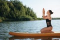 Young woman practicing yoga on color SUP board on river Royalty Free Stock Photo