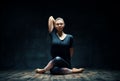 Young woman practicing yoga doing Gomukhasana, cow face pose, in dark room