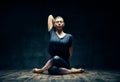 Young woman practicing yoga doing Gomukhasana, cow face pose, in dark room.