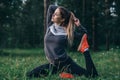 Young woman practicing yoga doing one-legged pigeon pose sitting on grass in park Royalty Free Stock Photo