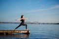 Young woman practicing yoga exercise at quiet wooden pier with city background. Sport and recreation in city rush Royalty Free Stock Photo