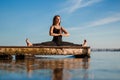 Young woman practicing yoga exercise at quiet wooden pier with city background. Sport and recreation in city rush Royalty Free Stock Photo