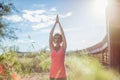 Portrait of young woman practicing yoga outdoors with hands raised up near the wooden bridge and plants. Upward Salute