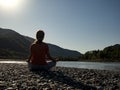 Young woman is practicing yoga in lotus pose at mountain lake Royalty Free Stock Photo