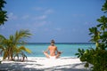 Young woman practicing yoga meditation on the beach facing the ocean near a palm tree on Maldives Royalty Free Stock Photo