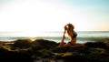 Young woman practicing yoga, sitting in Rajakapotasana pose on the beach. Sunset time. Tegal Wangi beach, Bali Royalty Free Stock Photo