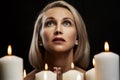 Young woman prays with candles. Beautiful blonde on a black background. Close-up