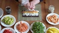 young woman prepares sushi with fresh ingredients at home. on wooden table.