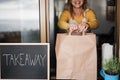 Young woman preparing takeaway food for fast delivery inside ghost kitchen - Focus on hands holding bag