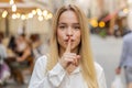 Young woman presses finger to lips makes silence hush sign do not tells gossip secret quiet in city Royalty Free Stock Photo