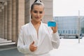 Young woman professional standing on a light background showing a credit card looking at camera showing thumb up smiling positive Royalty Free Stock Photo