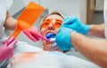 Young woman in protective eyeglasses during teeth composite filling material polymerization procedure with curing UV light at Royalty Free Stock Photo