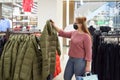 Young woman in protective mask chooses winter jacket in the store Royalty Free Stock Photo