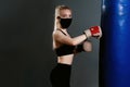 Young woman in a protective mask hits a punching bag