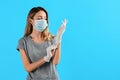 Young woman in protective mask putting on medical gloves against light blue background. Space for text Royalty Free Stock Photo