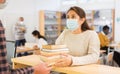 Young woman in protective mask returning books to to librarian