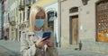 Young woman in protective mask using smartphone in the street of old city. Worried girl searching news about Covid-19